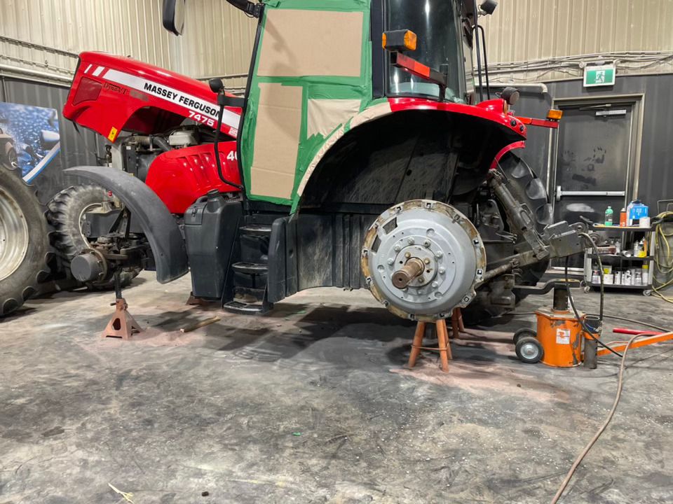 Un tracteur rouge et vert est en réparation dans un garage.