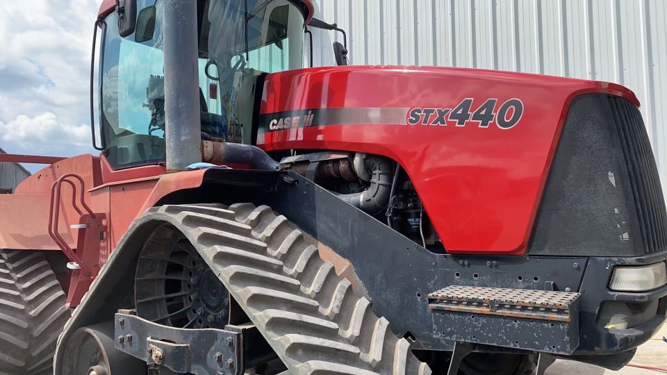 Un tracteur rouge est garé devant un bâtiment blanc.
