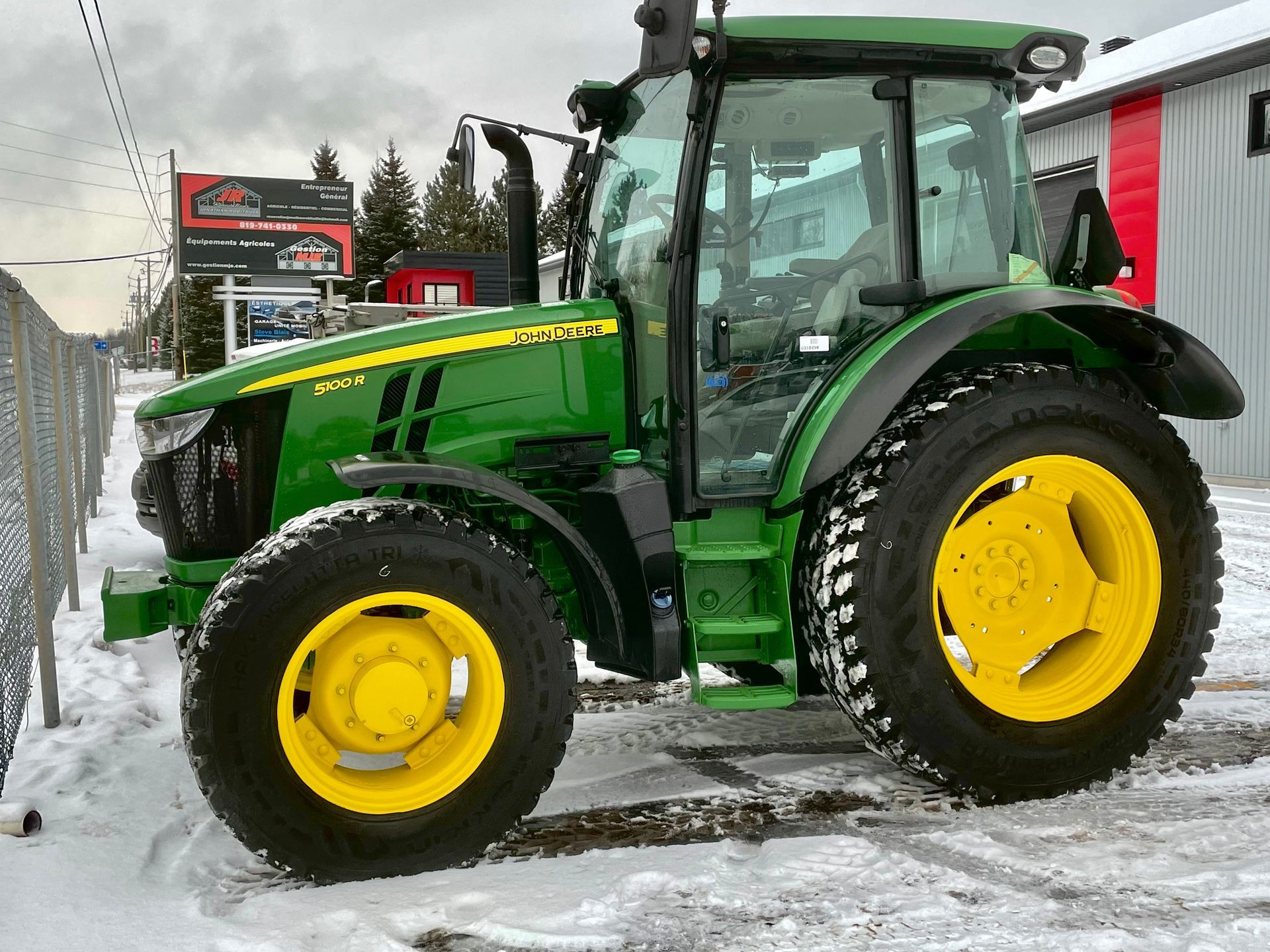 Un tracteur John Deere vert et jaune est garé dans la neige