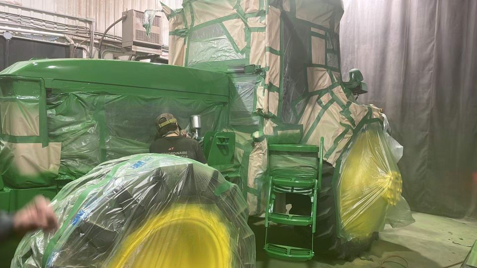 Un tracteur vert et jaune est peint dans un garage.