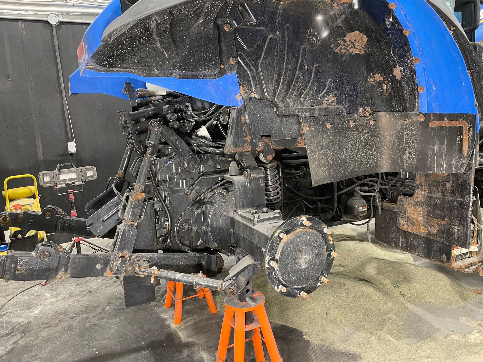 Un tracteur bleu et noir est assis sur des chandelles orange dans un garage.