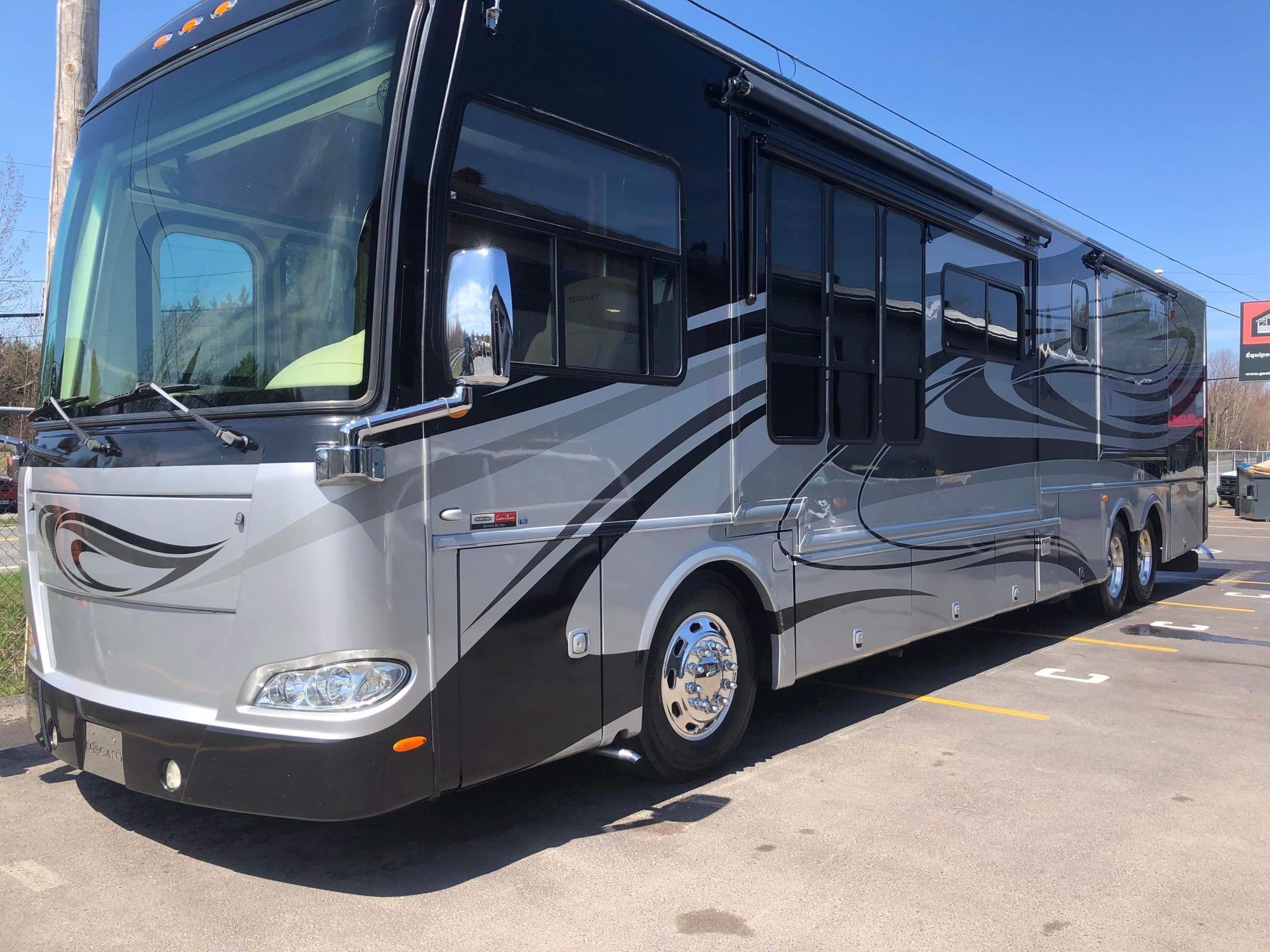Un grand camping-car argenté et noir est garé dans un parking.