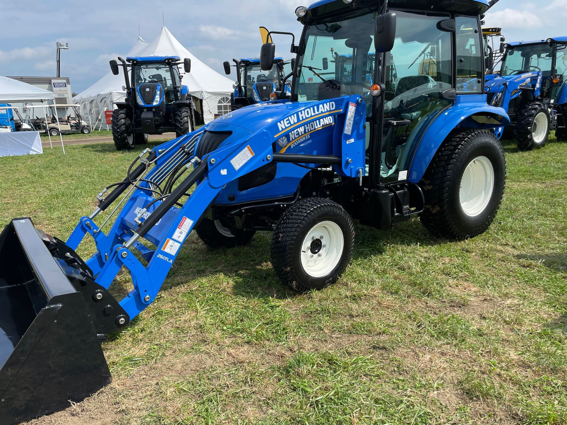 Un tracteur bleu avec un chargeur frontal est garé dans un champ herbeux.