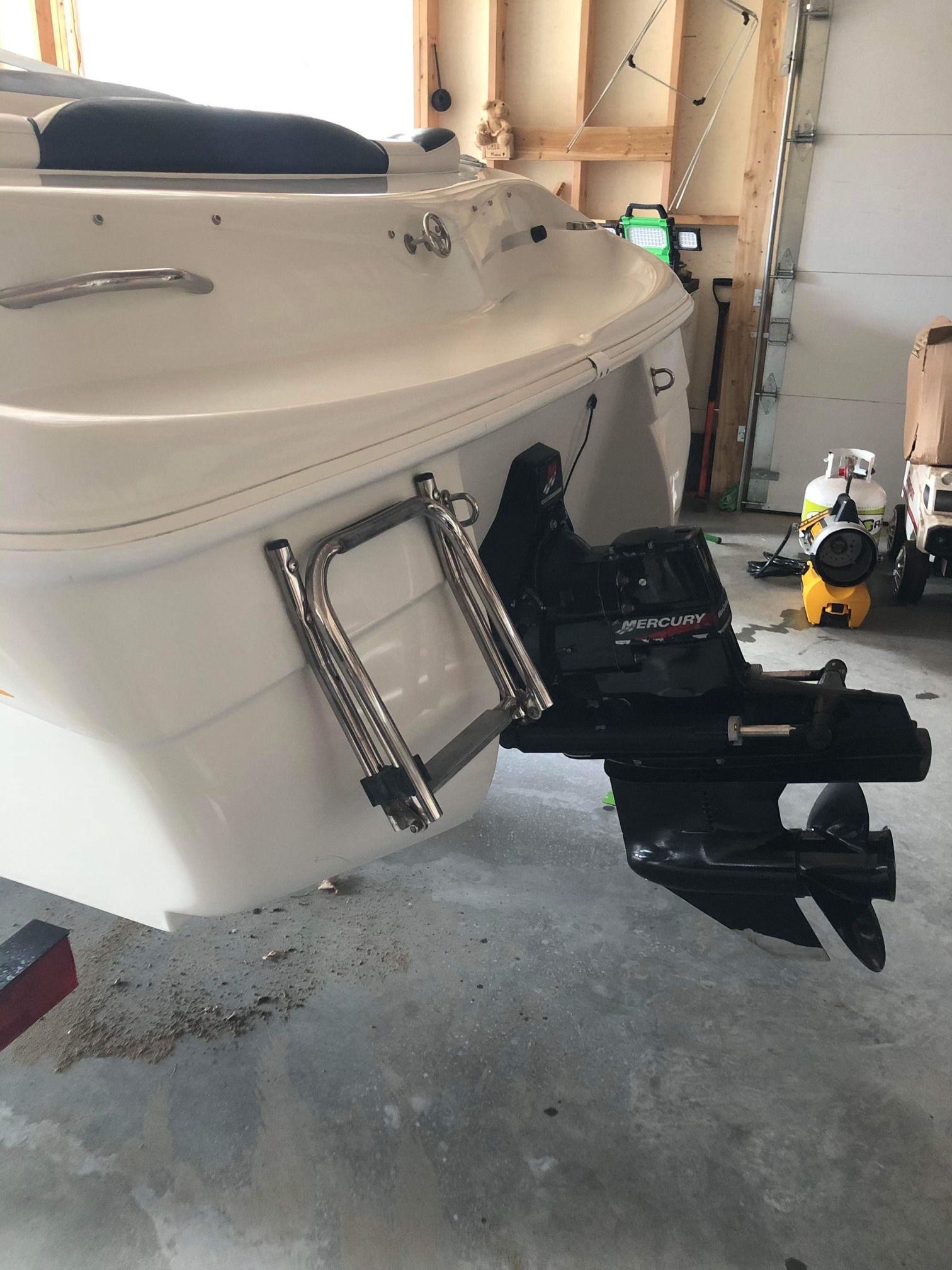 Un bateau blanc est garé dans un garage à côté d’un moteur hors-bord au mercure.