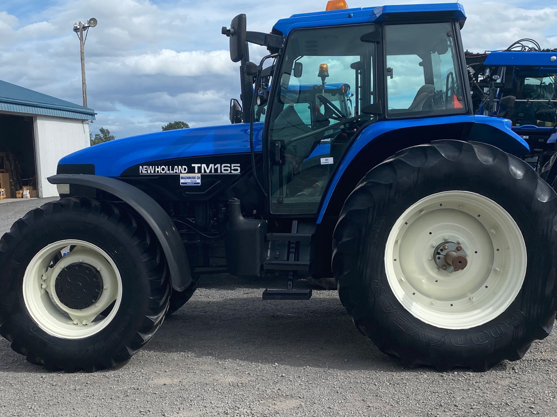 Un tracteur New Holland bleu est garé dans un terrain de gravier