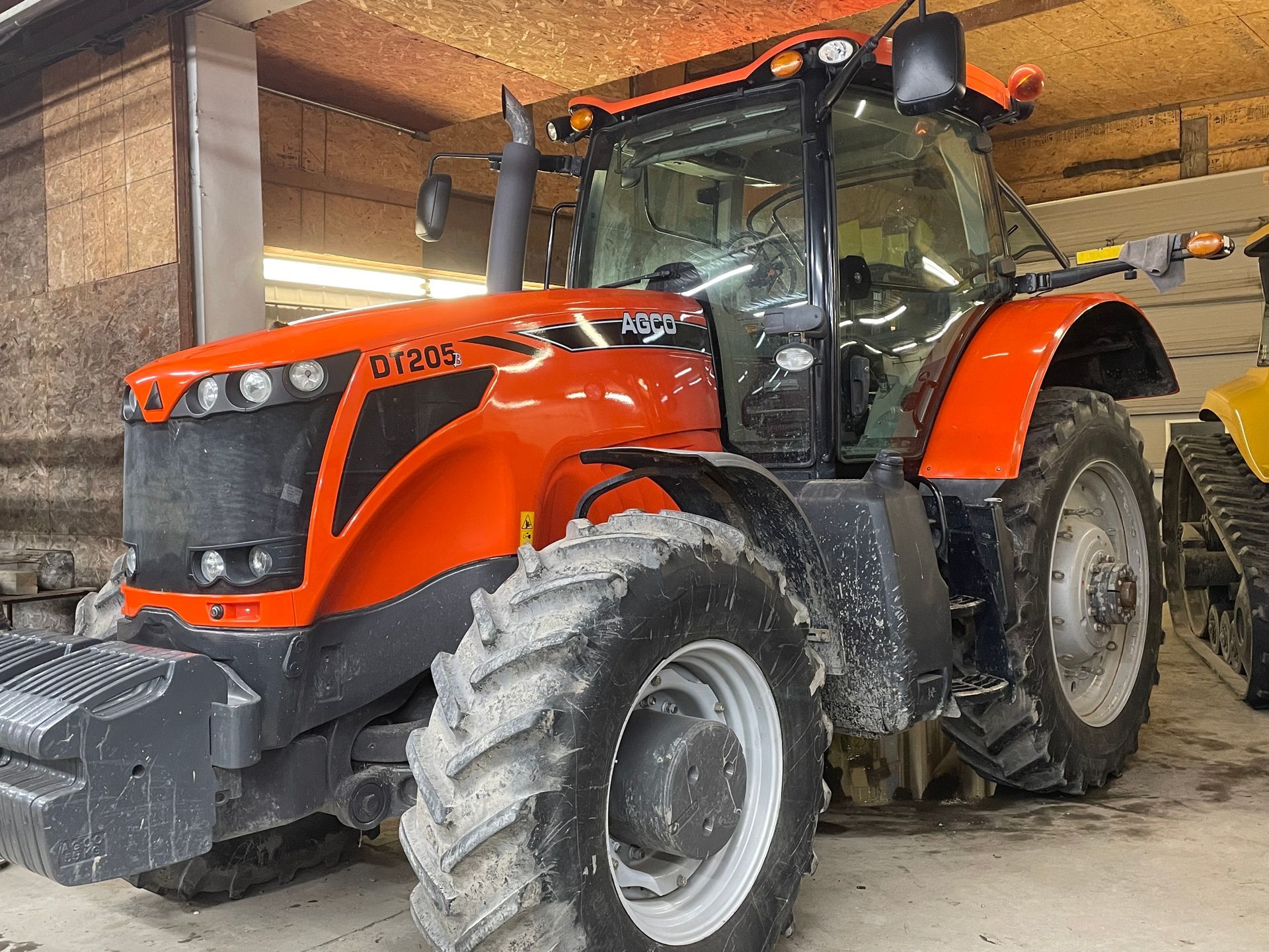 Un gros tracteur orange est garé dans un garage.
