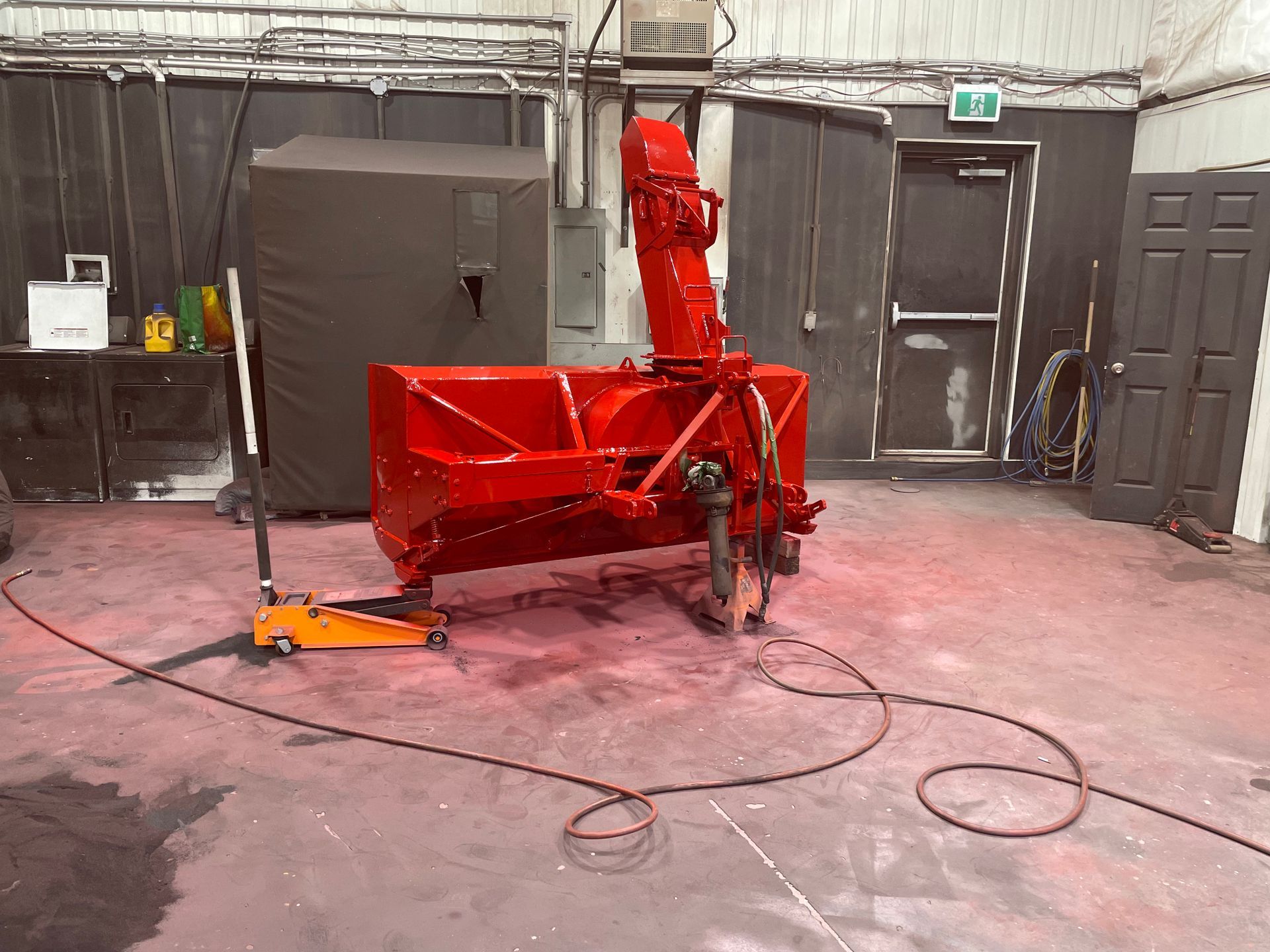 Une souffleuse à neige rouge est posée sur un cric dans un garage.