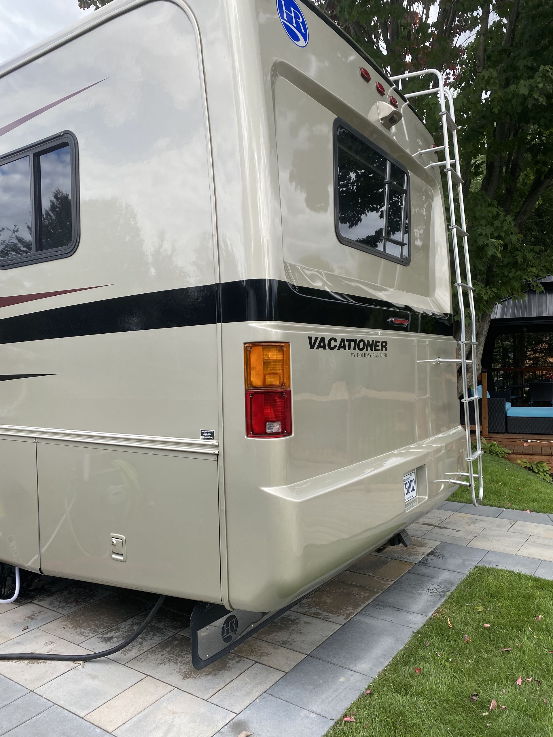 Un camping-car blanc avec une échelle attachée à l'arrière est garé dans une allée.