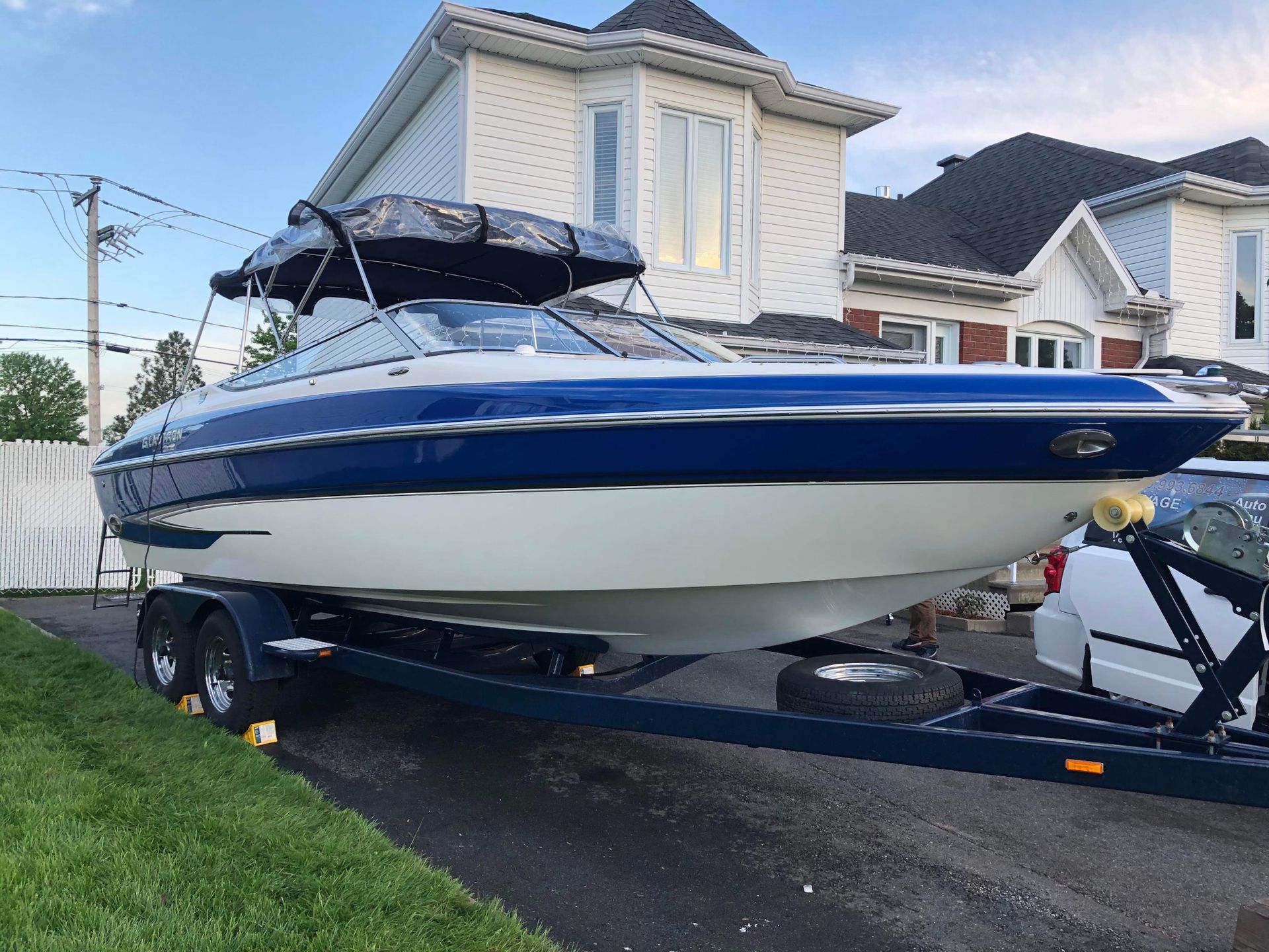 Un bateau bleu et blanc est sur une remorque devant une maison.