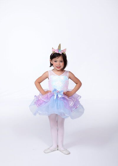 Girl in unicorn costume with tutu, headband, white tights, and ballet shoes.