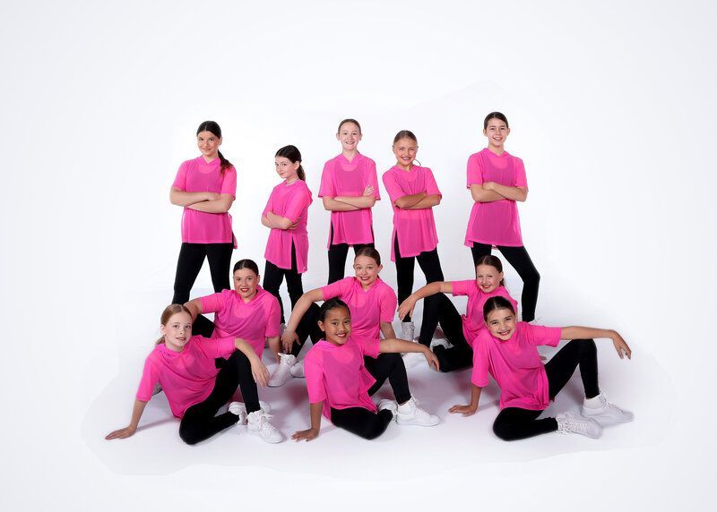 Group of children in pink shirts and black pants, posing for a photo.