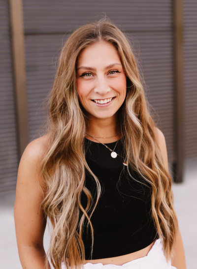 Woman with long, wavy blonde hair, smiling at camera; wearing black top and white bottoms.