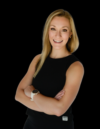 Blonde woman in black sleeveless top smiles, arms crossed against black backdrop.