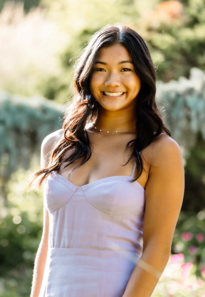 Woman in lavender dress smiles outdoors.