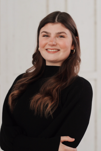 Woman with brown hair smiles, wearing a black turtleneck in a bright room.