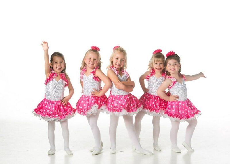 Five young dancers in pink and white costumes pose, smiling.