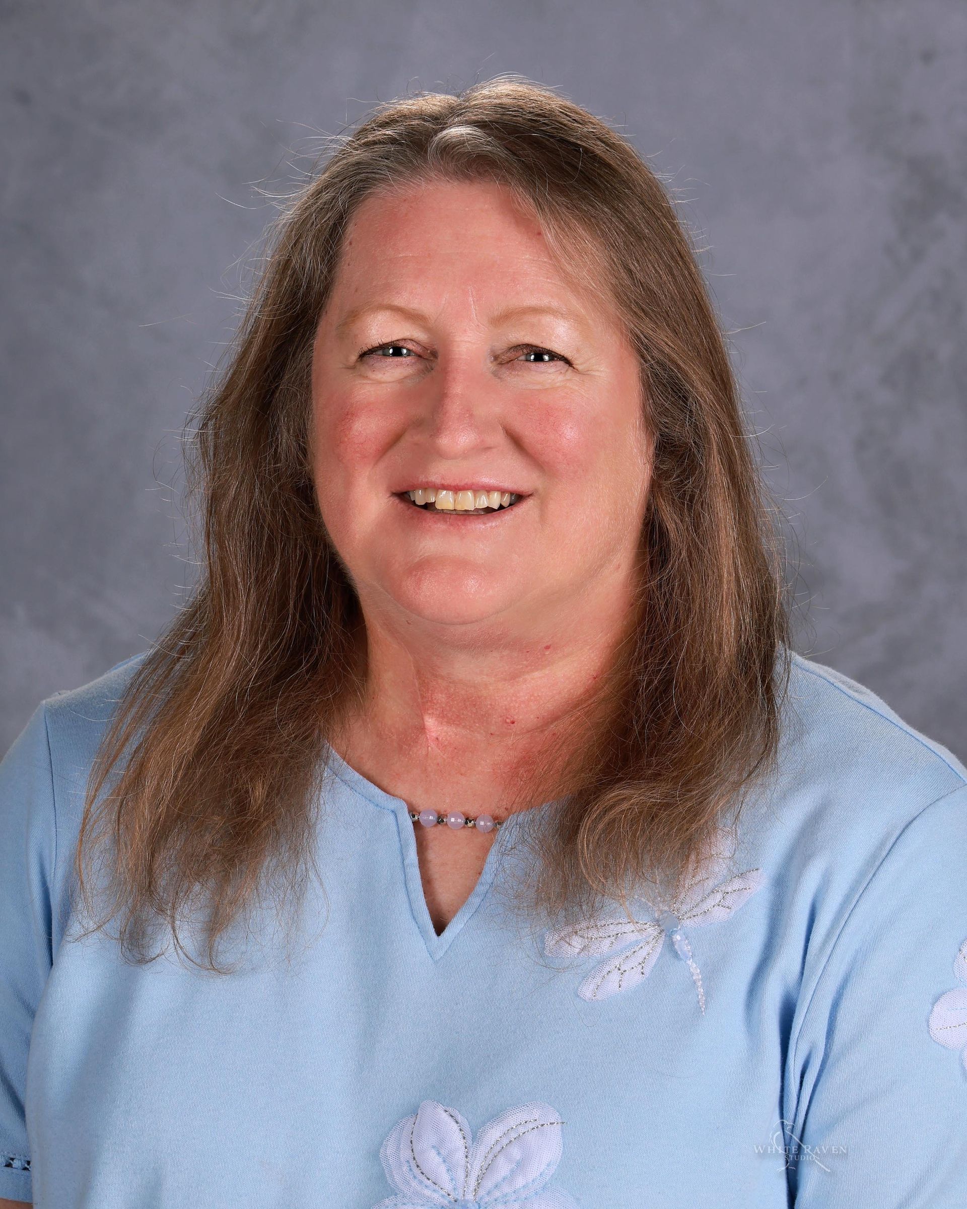 A woman wearing a blue shirt and a necklace is smiling for the camera.