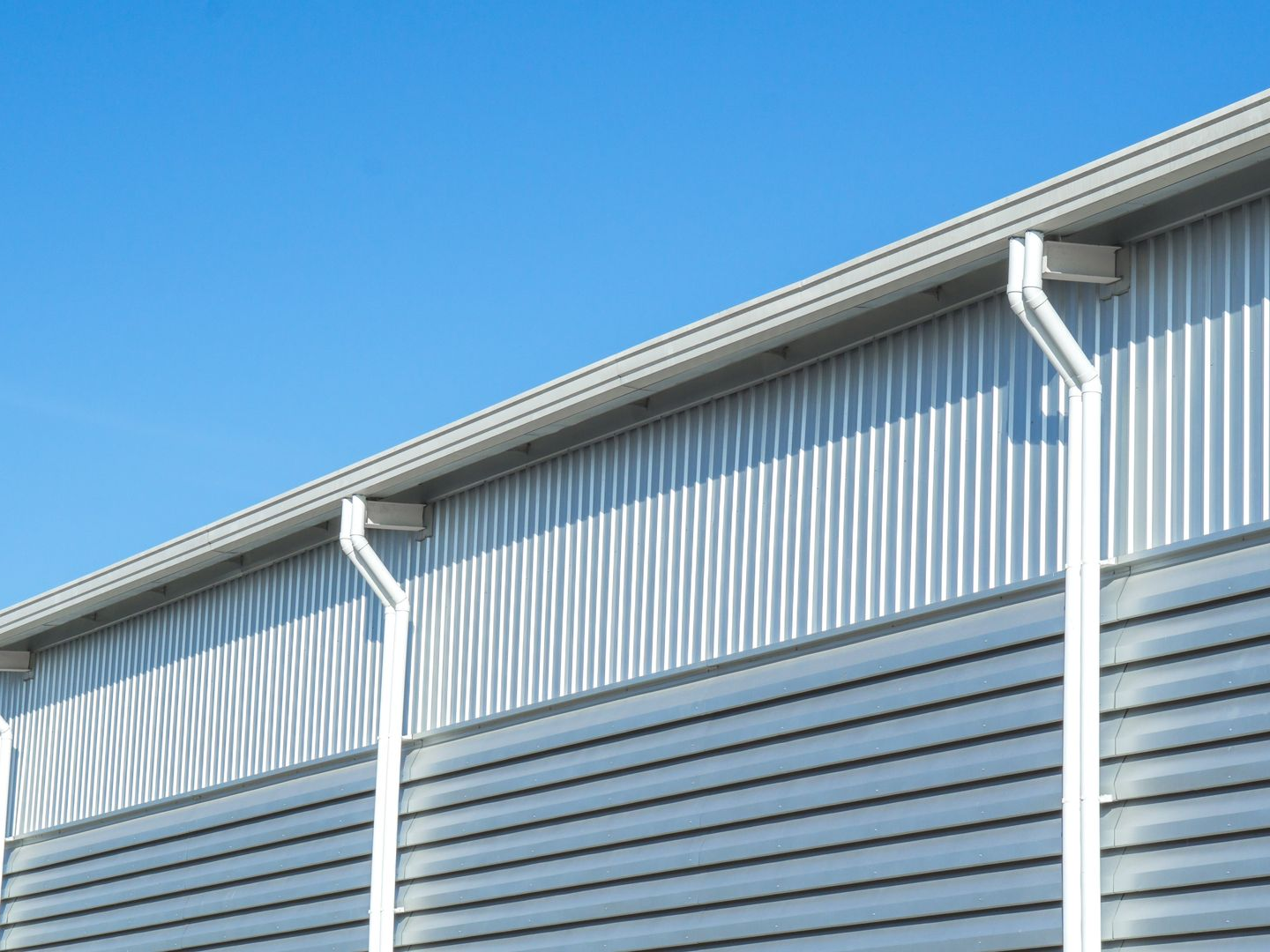 Metallic building exterior with white gutters against a blue sky.