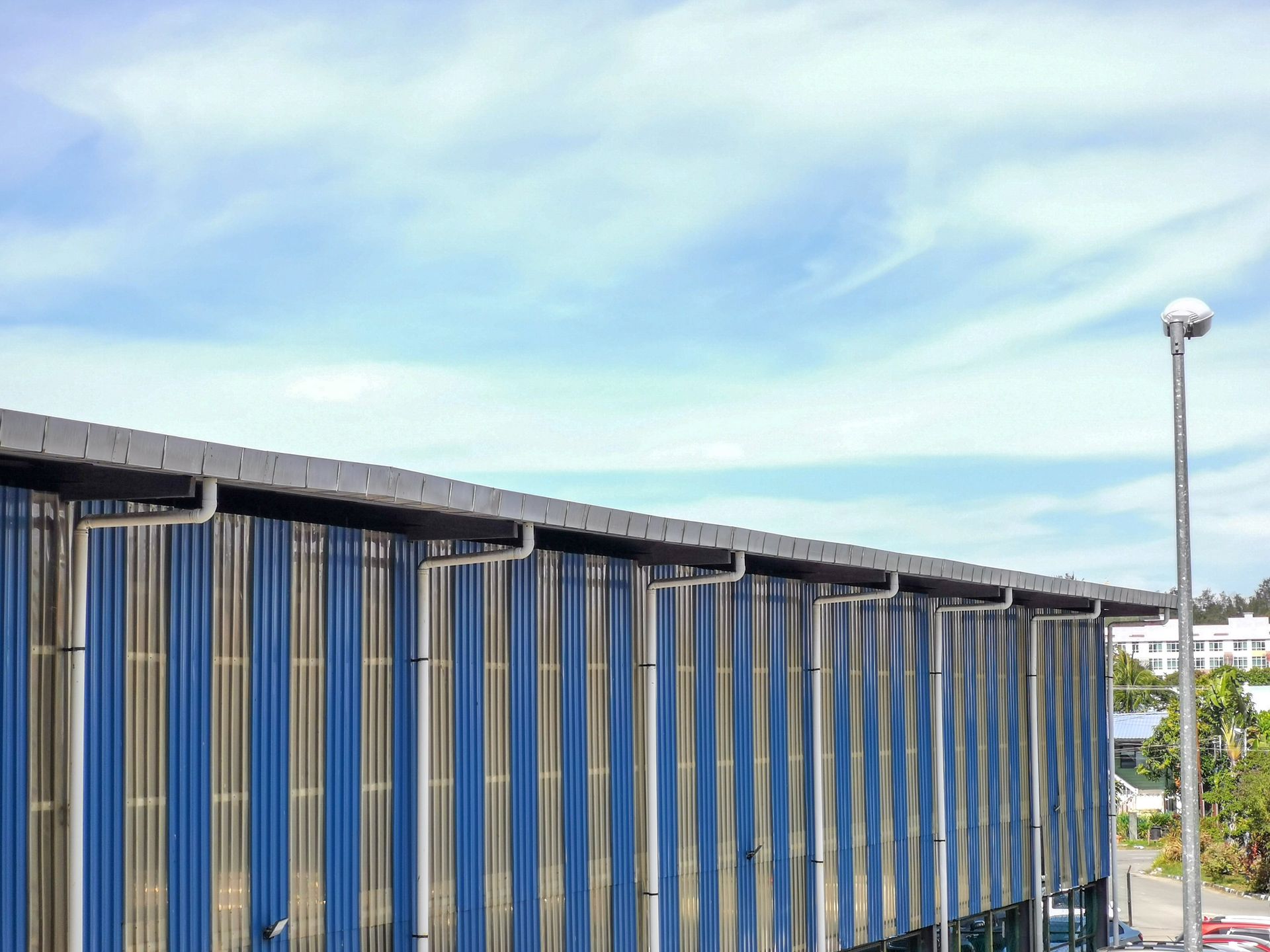 Blue and silver corrugated metal building with a rain gutter under a cloudy blue sky.