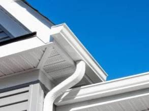 White rain gutter and downspout on a house with blue sky backdrop.