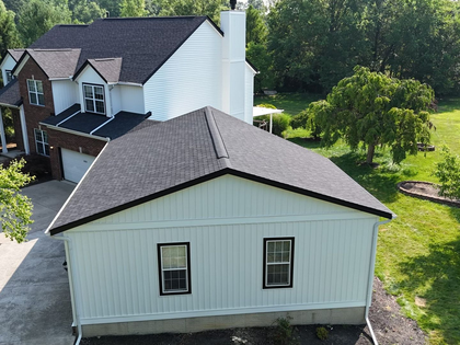 White house with black roof and trim; detached garage, brick facade, trees.