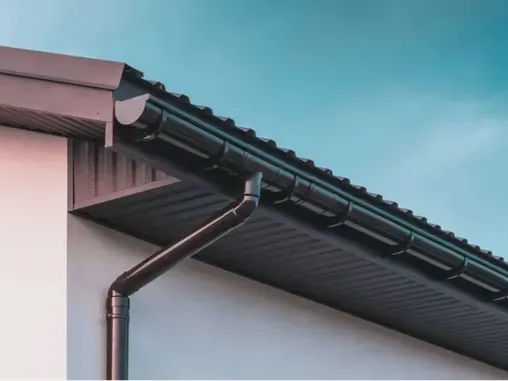 Black gutters along a roofline, with a downspout.