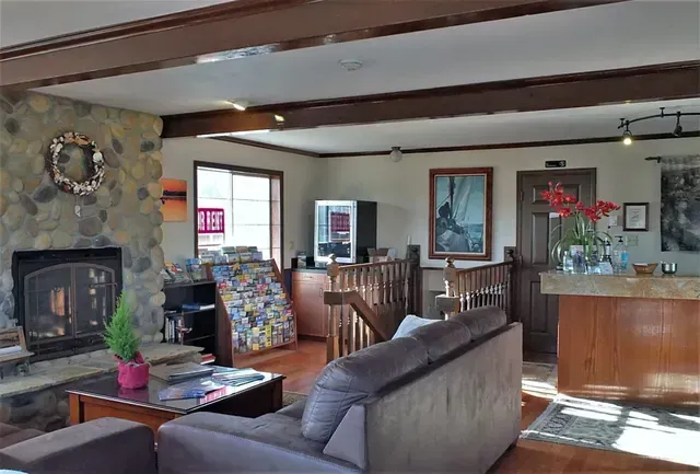 A cozy lobby featuring a stone fireplace, a gray sofa, a wood coffee table, and a reception desk in a brightly lit room.
