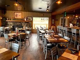 A dining room featuring wooden tables and metal chairs, with a stone fireplace and large window in the background.