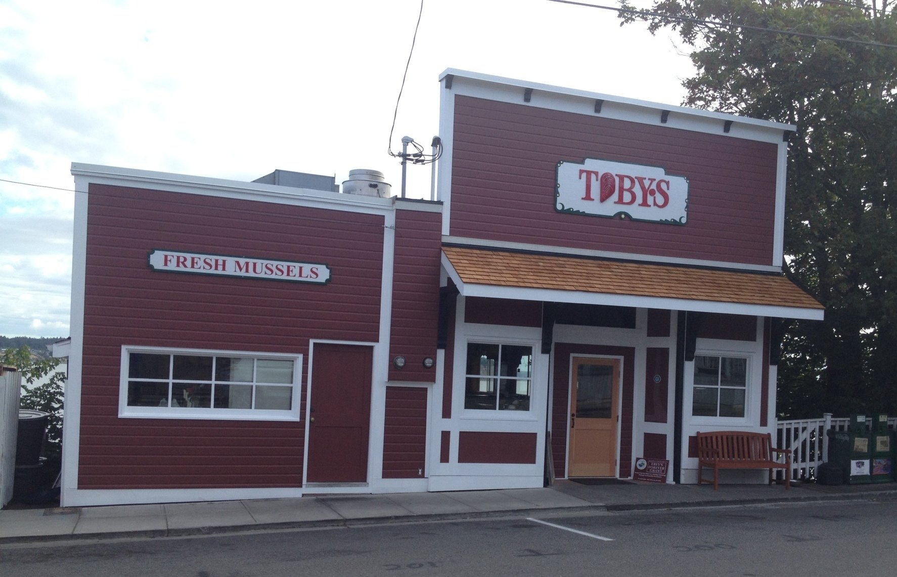 A two-story red, rustic-style building called Toby’s, featuring a sign for “Fresh Mussels” on its smaller side wing.