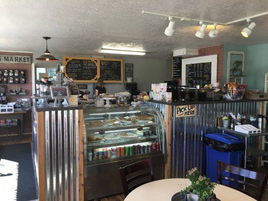 Interior of a cafe with a metal-paneled service counter, glass display case, menu boards, and seating area.