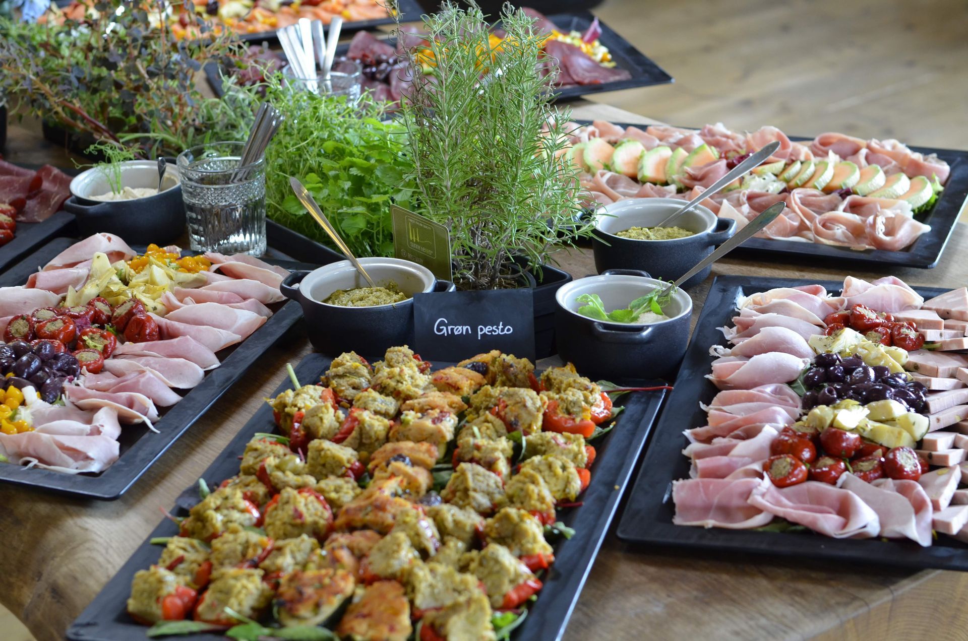 Et bord med sorte bakker med forskellige forretter, herunder kød, ost og spyd, arrangeret til buffet.