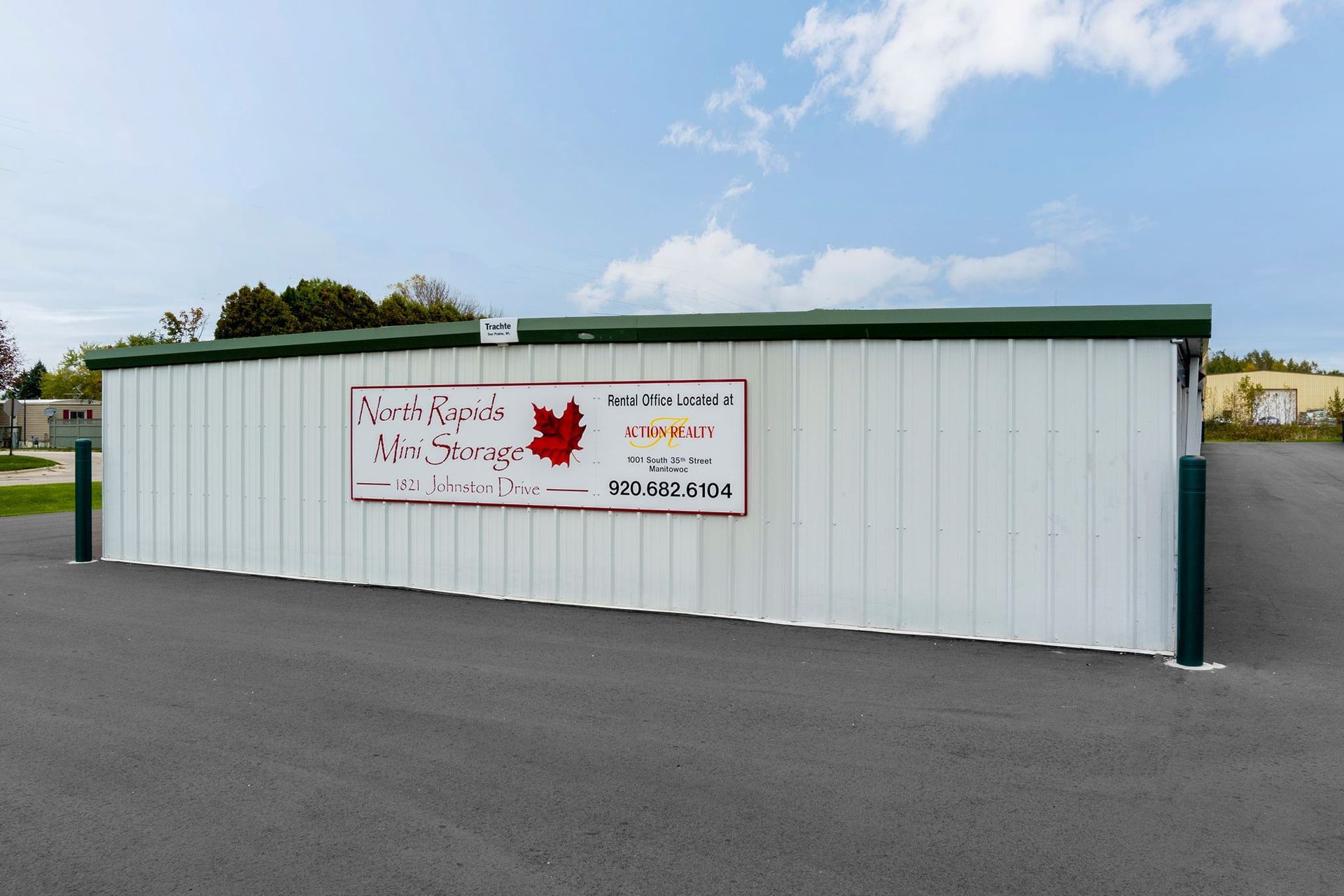 White metal building with sign, maple leaf logo, parked on blacktop.