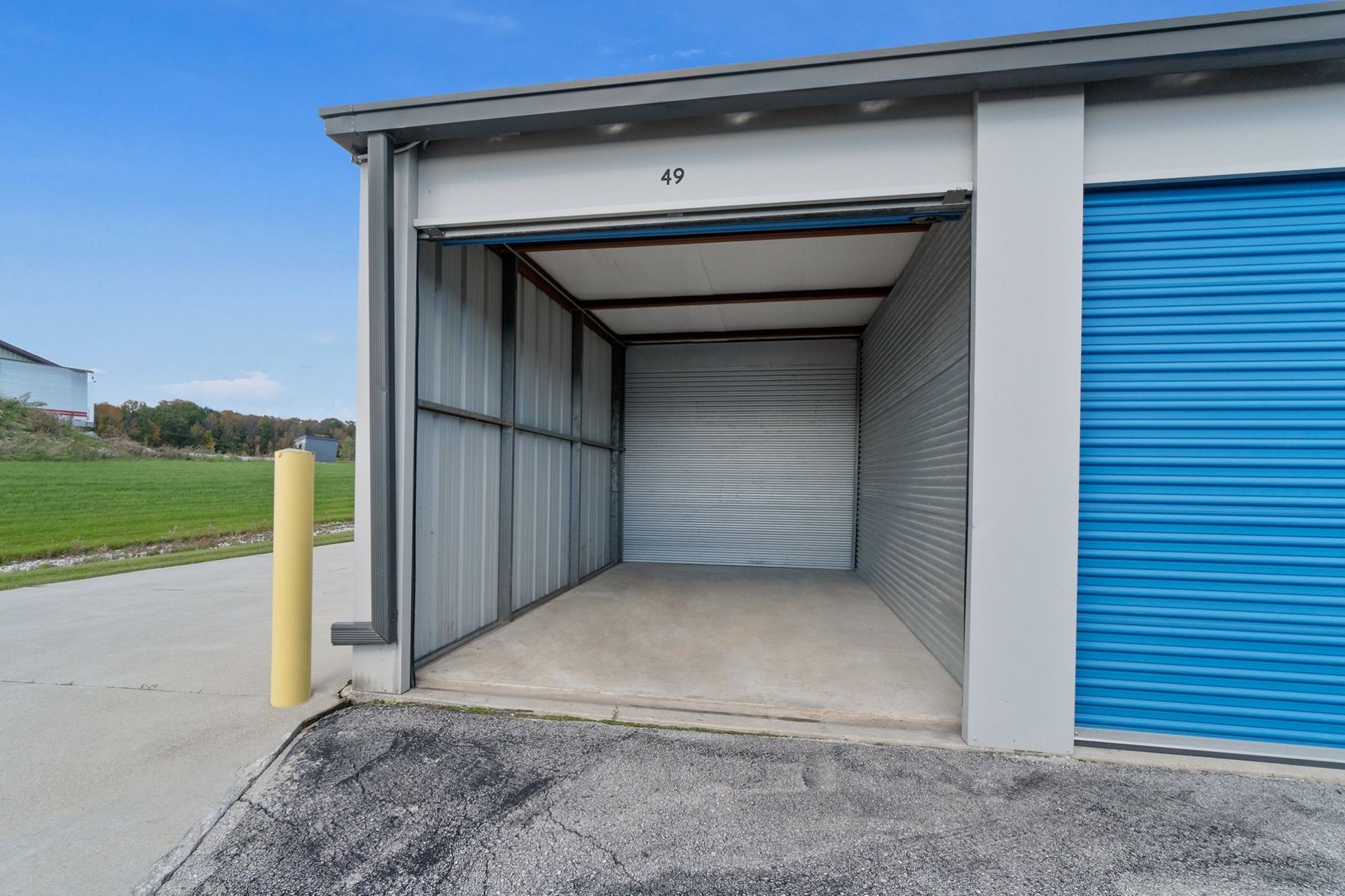 Open storage unit with a blue door, exterior concrete with grass and sky.