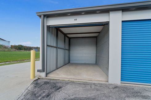 Open storage unit with a blue door, gray walls, and concrete floor.