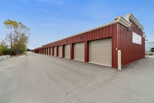 Red storage units with beige doors along a concrete driveway, under a blue sky.