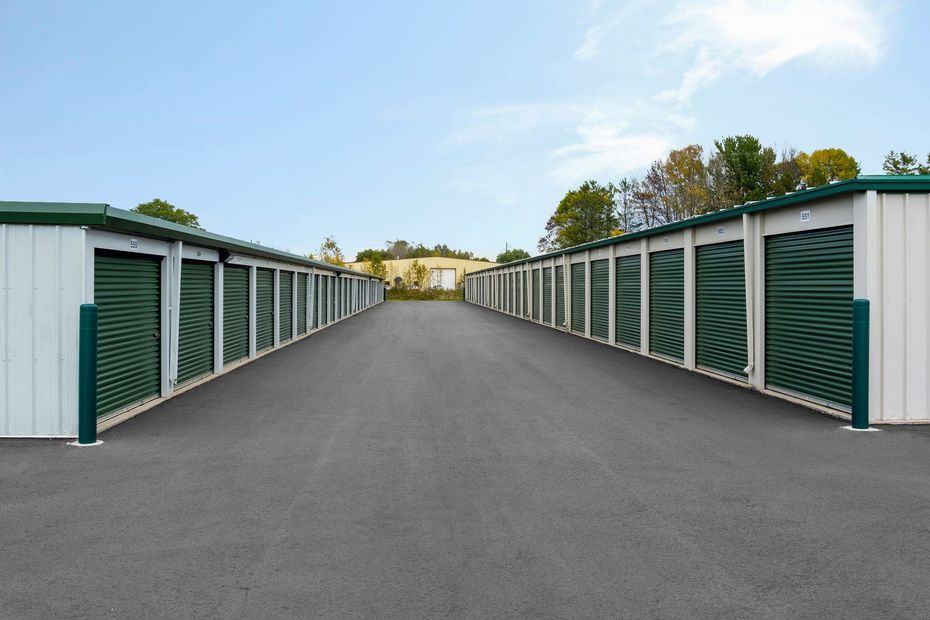 Storage units with green doors line a gray asphalt drive under a blue sky.
