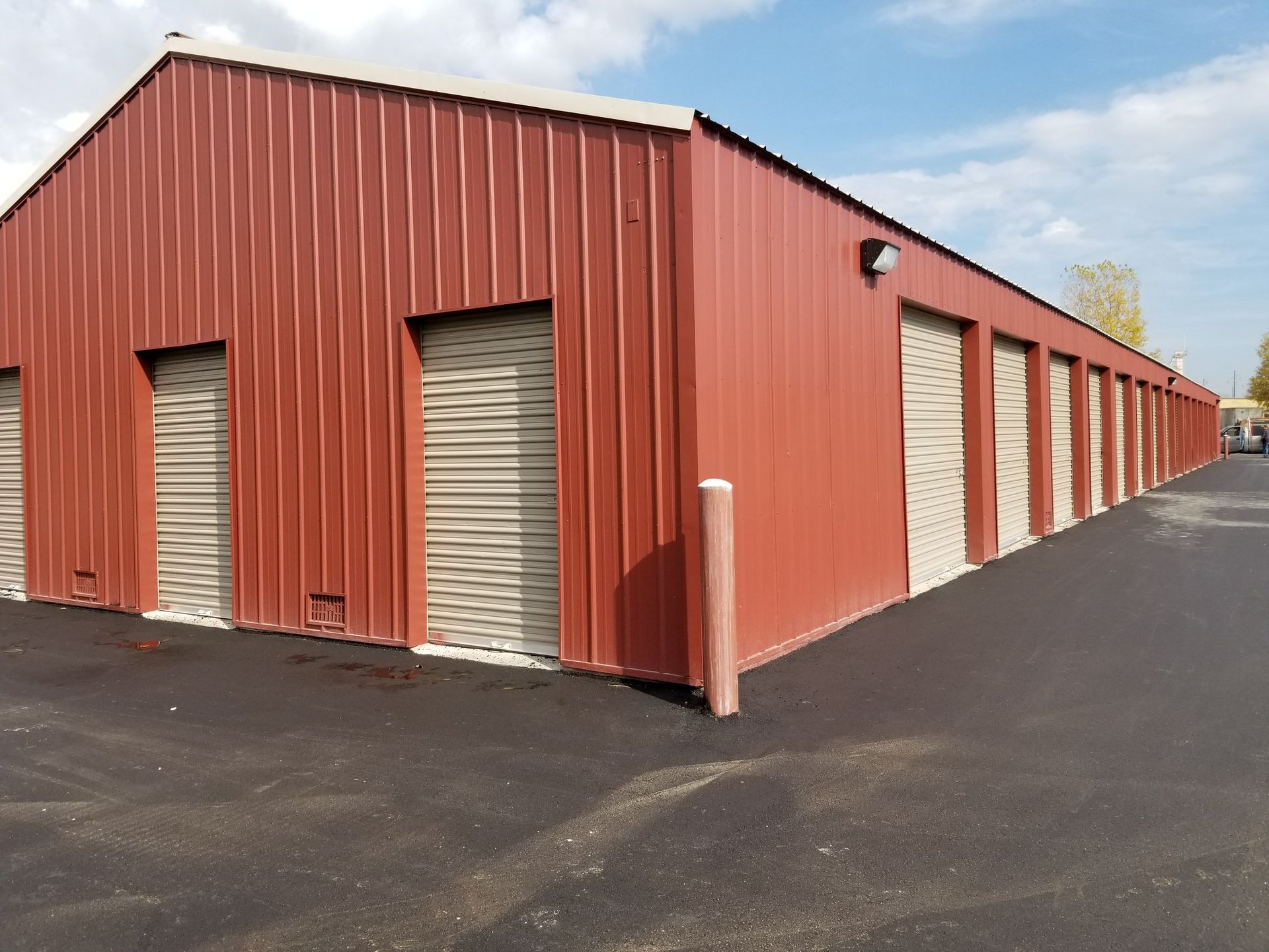 Red metal storage units with tan doors, asphalt parking.