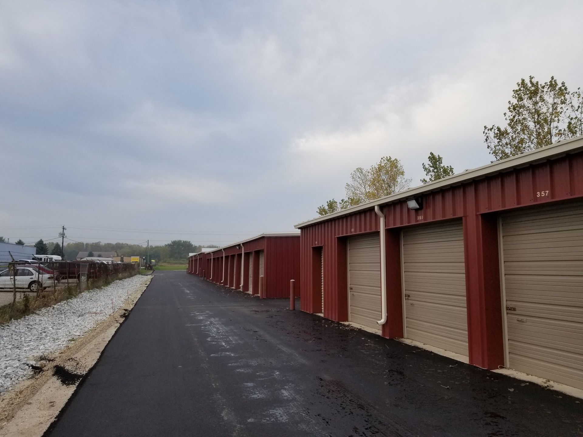Storage units in a row, with red siding and tan doors, under a cloudy sky.