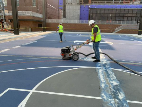Worker using a grinding machine to prepare a sport court surface before resurfacing during a court installation service in Peoria, AZ
