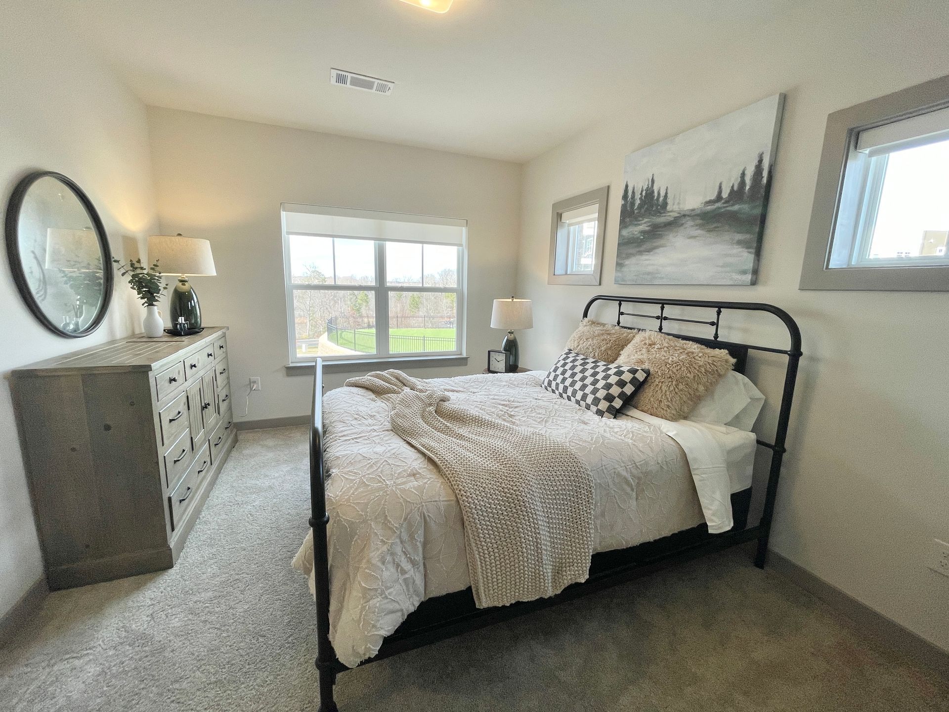 A bedroom with a bed , dresser , mirror and window.