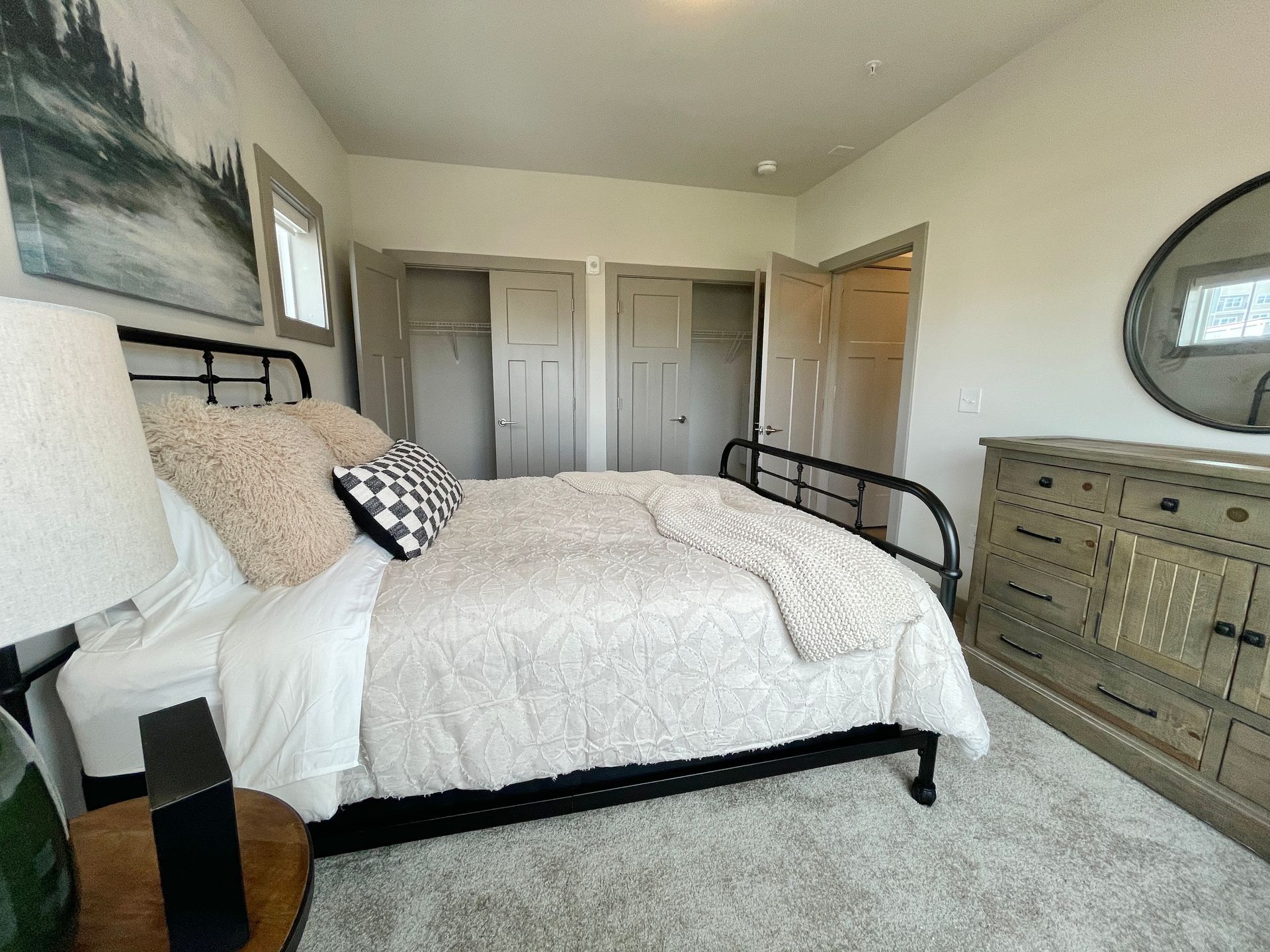 A bedroom with a bed , dresser , lamp and mirror.