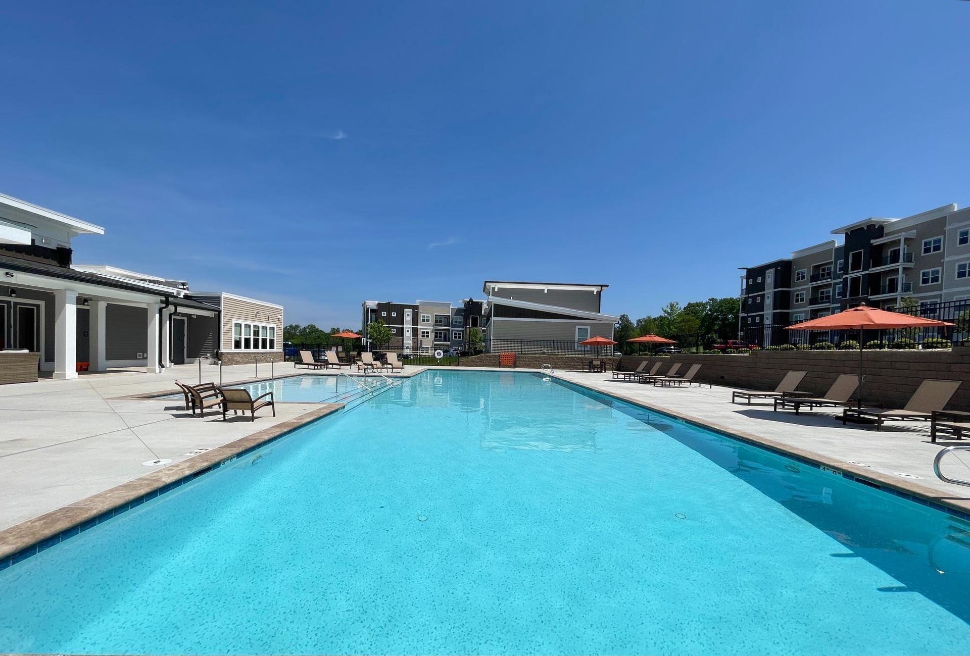 A large swimming pool surrounded by chairs and umbrellas in front of a building.