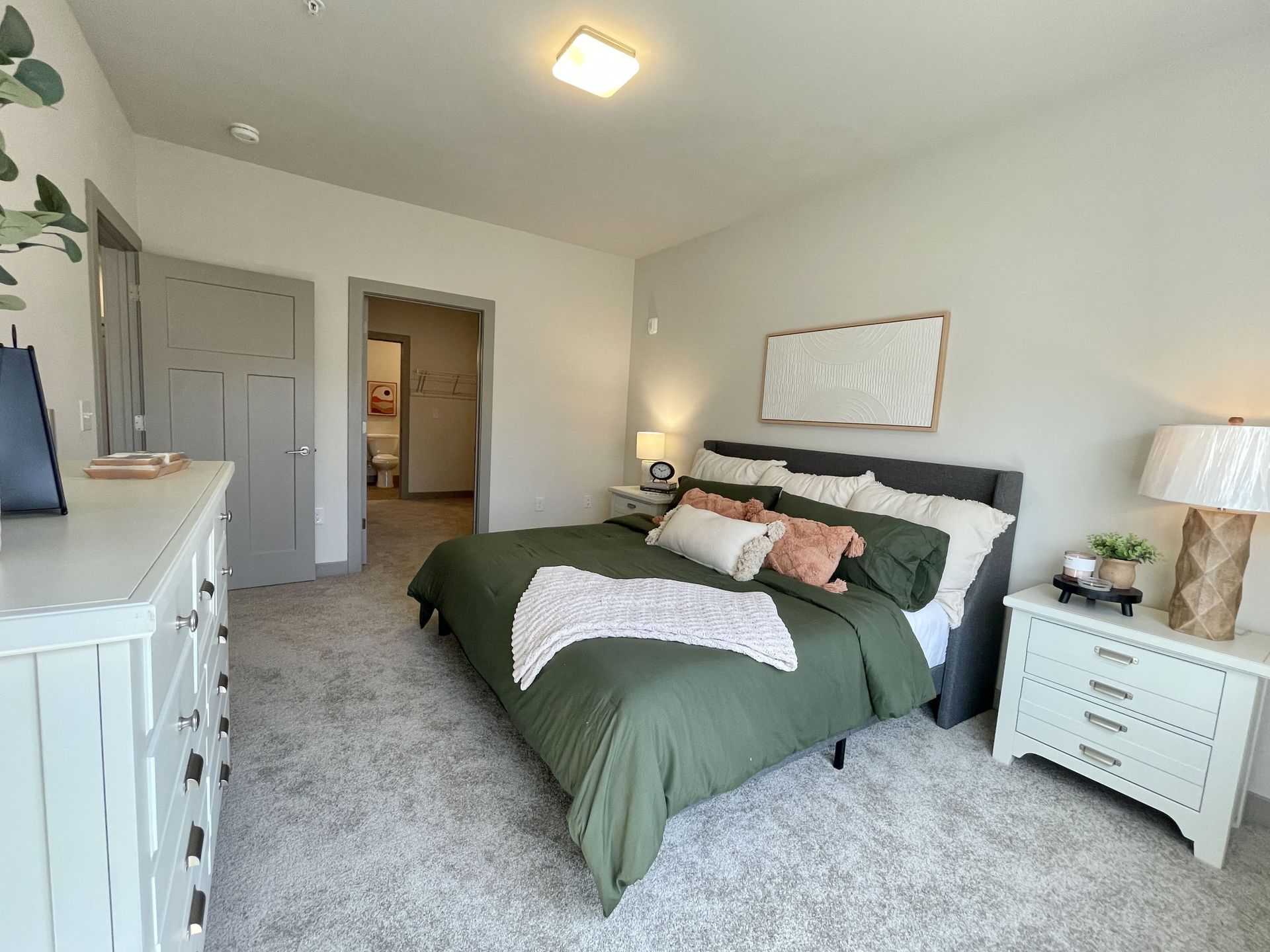 A bedroom with a large bed , dresser , nightstand and lamp.