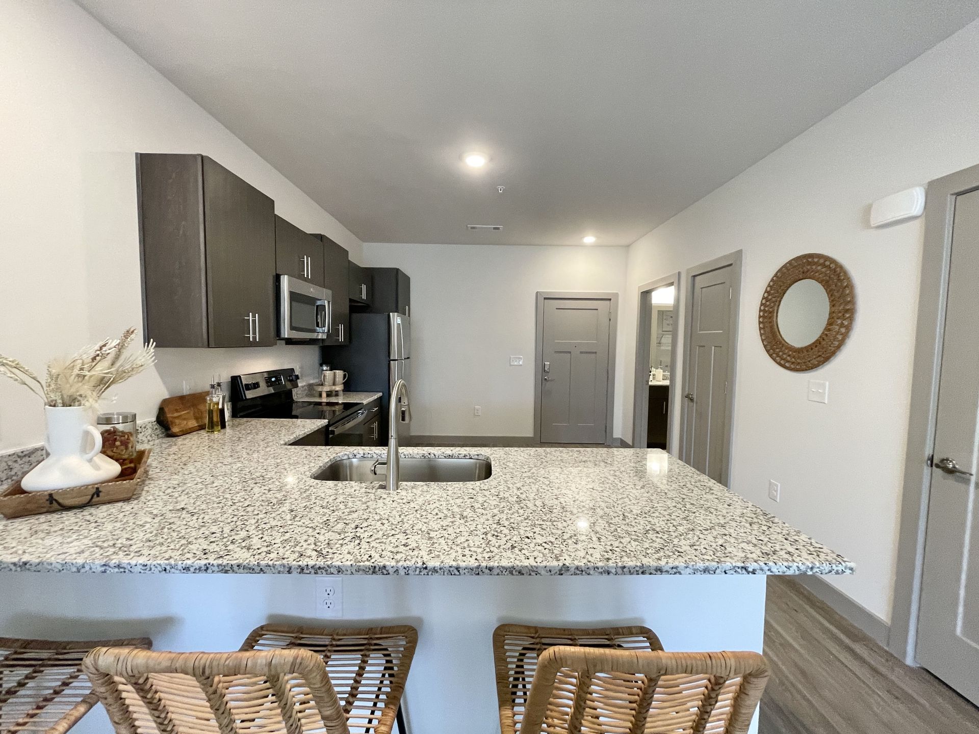 A kitchen with a granite counter top , stools , a sink and a microwave.