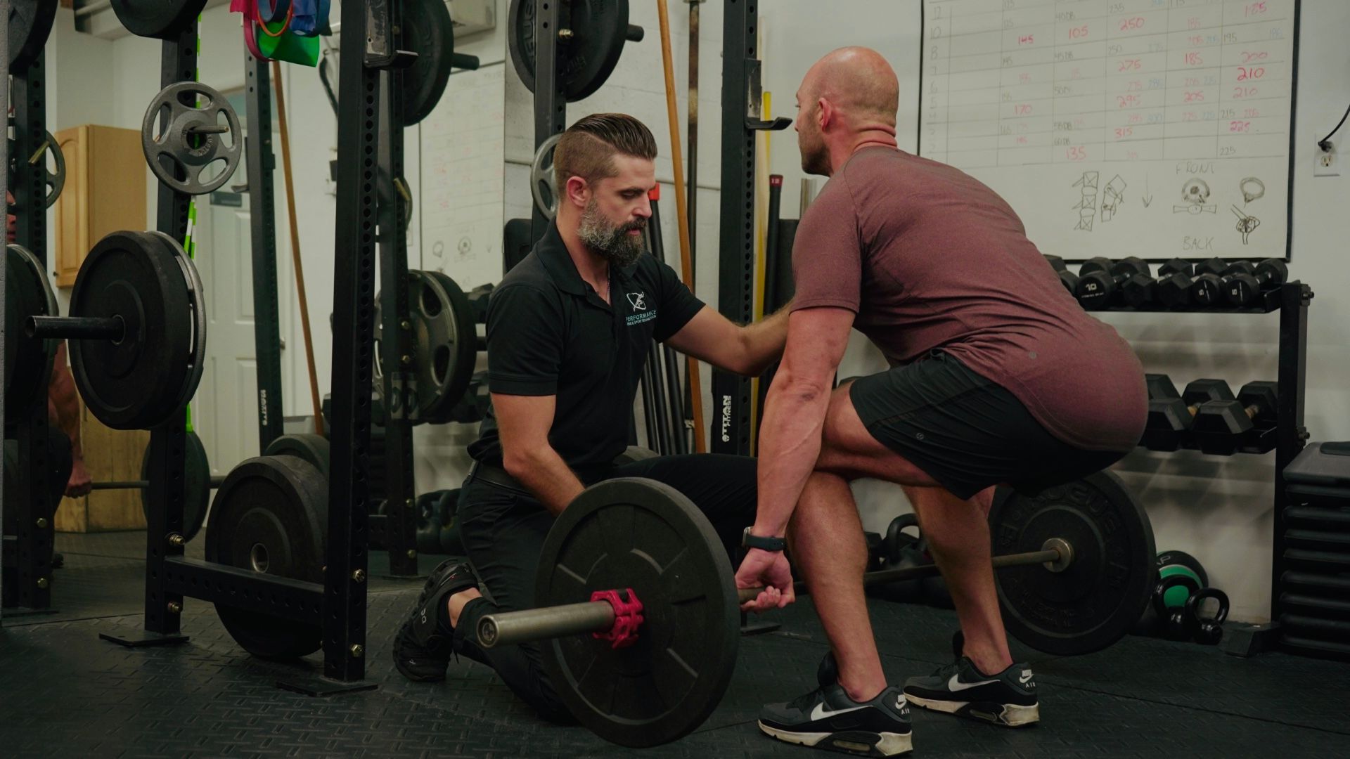 Trainer spotting a man doing a barbell lift in a gym.