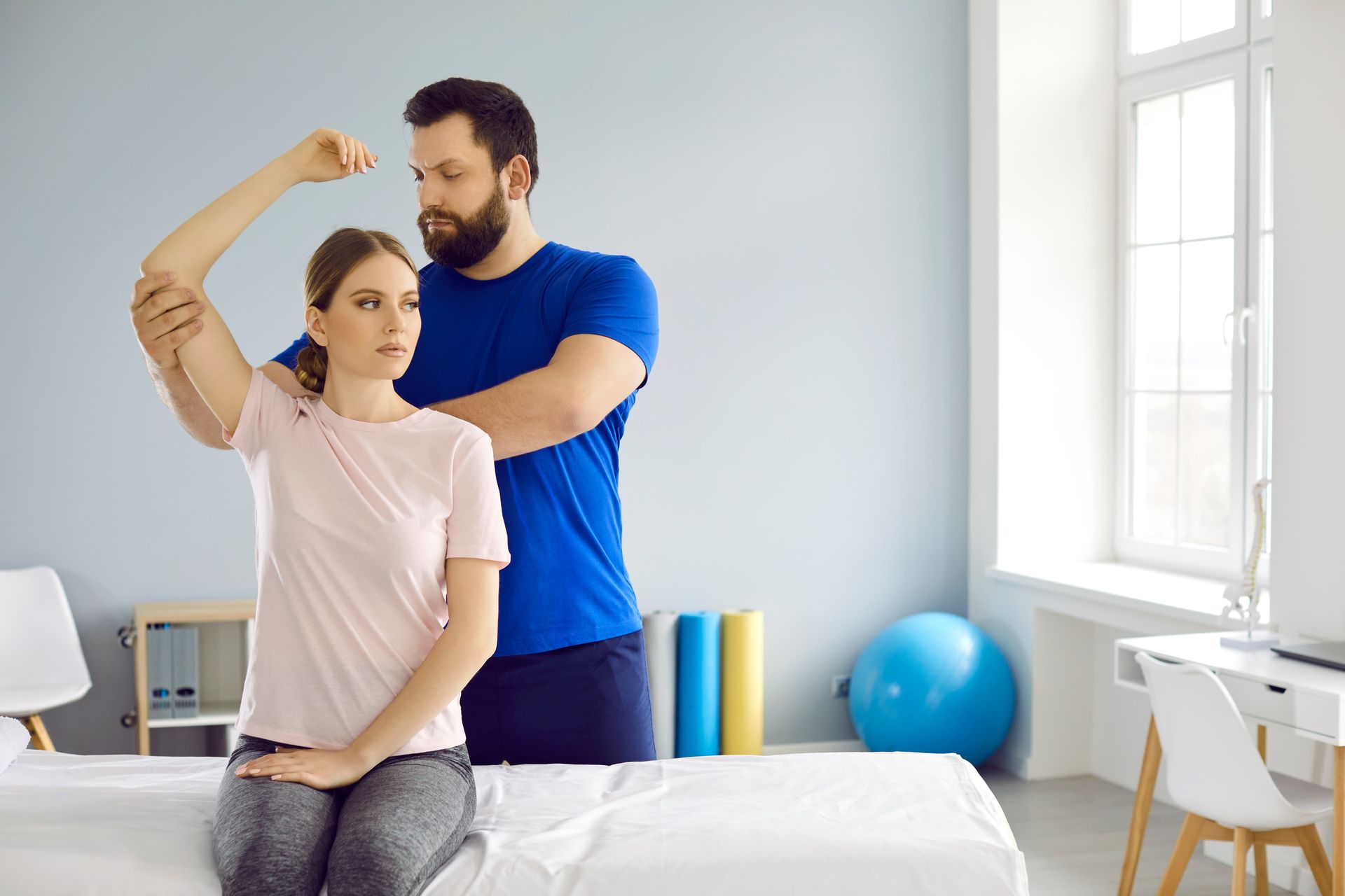 Therapist assisting a patient with arm movement in a medical office.