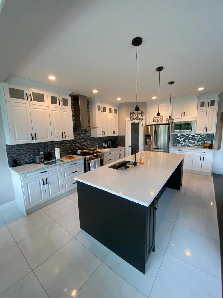 Modern kitchen with white cabinets, dark island, and stainless steel appliances.