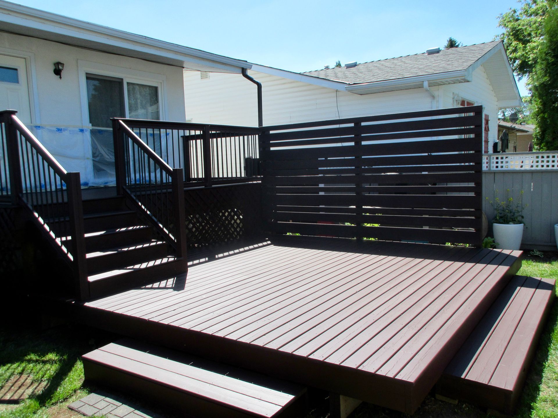 Brown composite deck with steps, railing, and privacy screen against a white house.