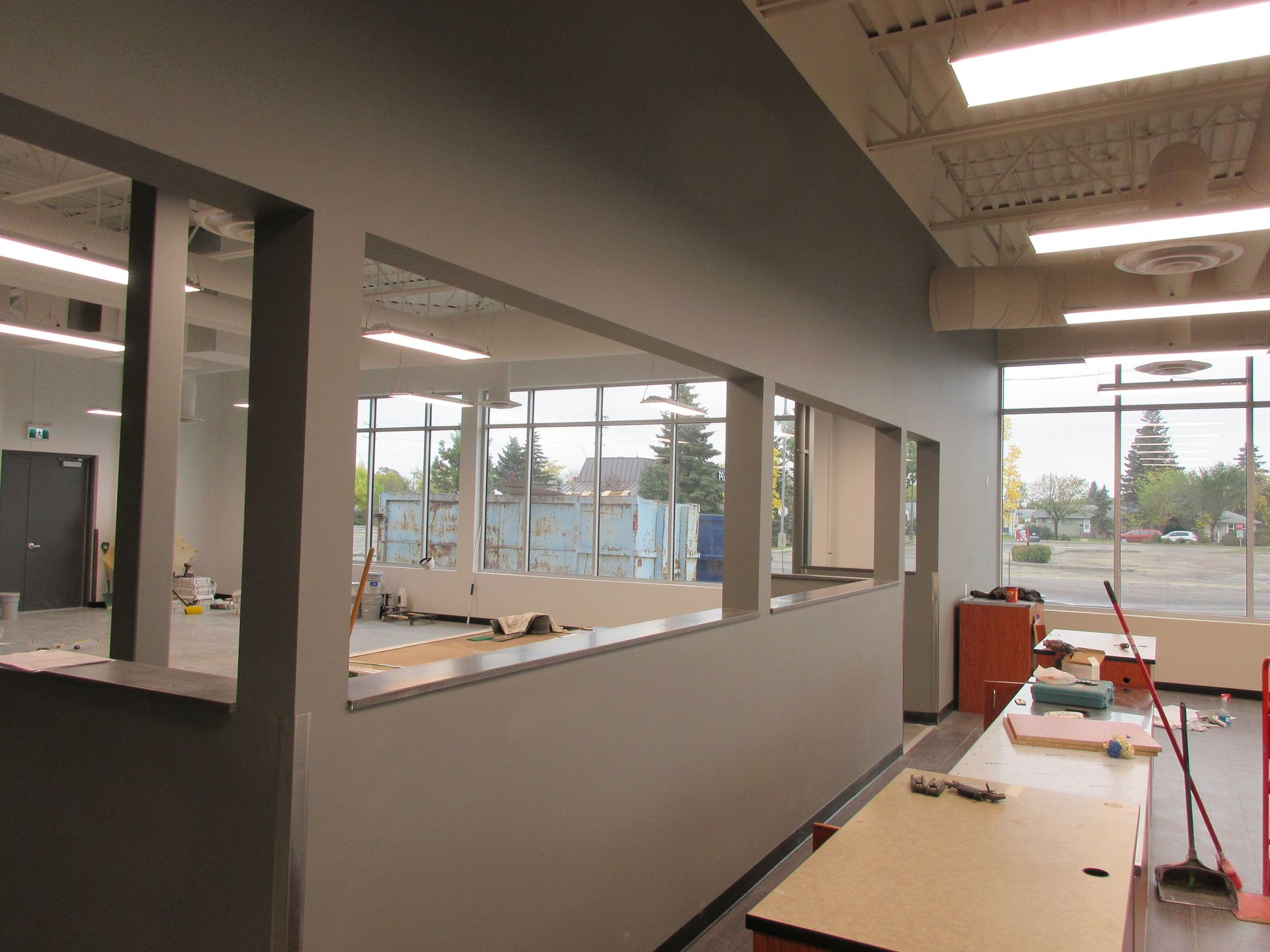 Interior view of a room with gray walls and large windows, containing work tables and construction materials.