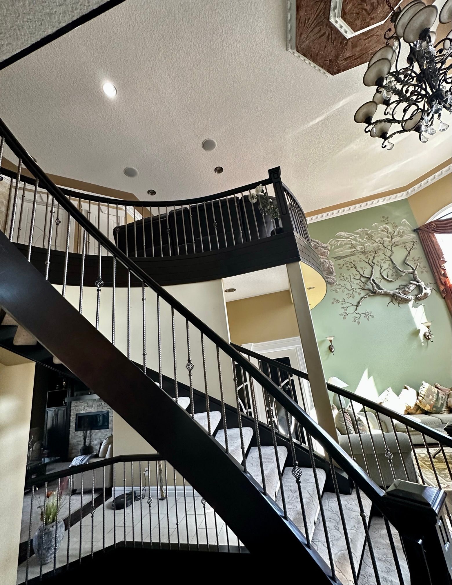 Dark wood staircase with metal railings, ascending to a second floor. A chandelier hangs from the ceiling.